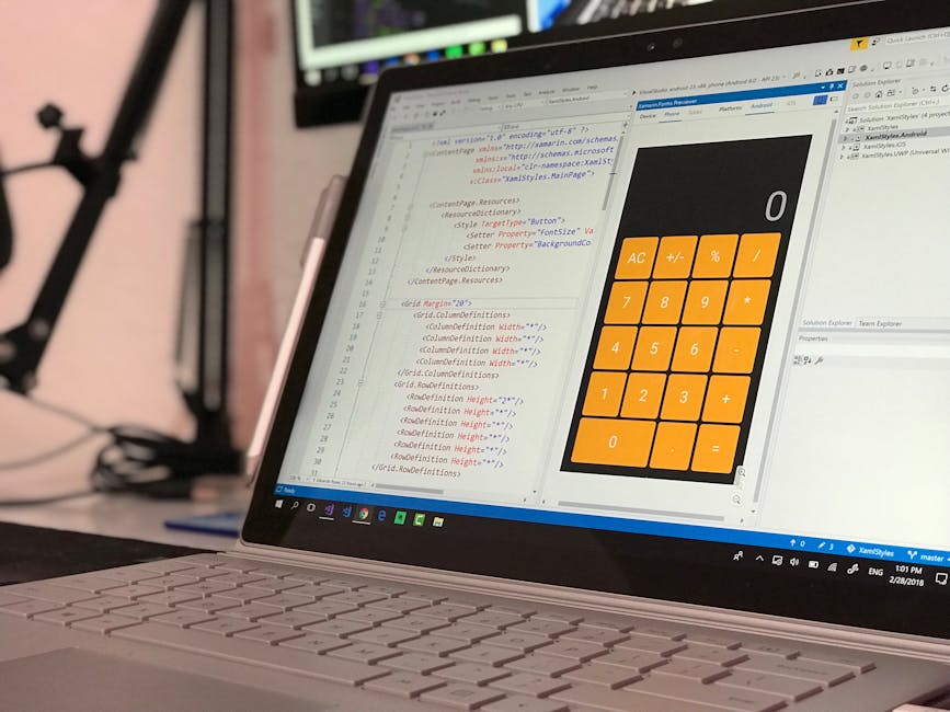 A close-up view of a laptop computer placed on a desk, displaying lines of code in a text editor on the left side of the screen and a digital calculator interface with large orange buttons on the righ